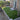 A backyard patio setup with bright green artificial turf, a gray wooden fence, brick house exterior, white French doors, and trees in a residential outdoor setting.