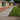 A backyard patio and lawn scene with a beige stucco house on the left, a paved walkway, green grass, trees, and blue sky.