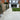 Backyard with paved patio, grass area, and potted plants.
