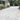 Paved driveway leading to a house with greenery and a car in the background; Dove Grey Limestone Block Paving