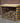 A wooden firewood storage rack filled with logs, positioned outdoors against a red brick wall and gravel ground.
