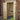 A tall wooden garden shed with two open doors, shown outdoors against a red brick wall. Inside, garden tools including shovels, a rake, and buckets are stored, along with some gardening products on the floor.
